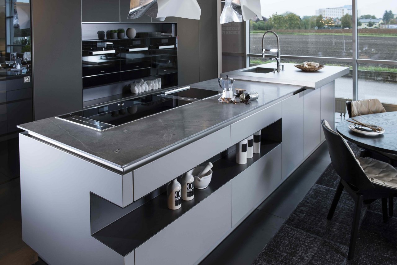 Offene, moderne Küche mit einer Arbeitsplatte aus grauem Naturstein und matten Küchenfronten.