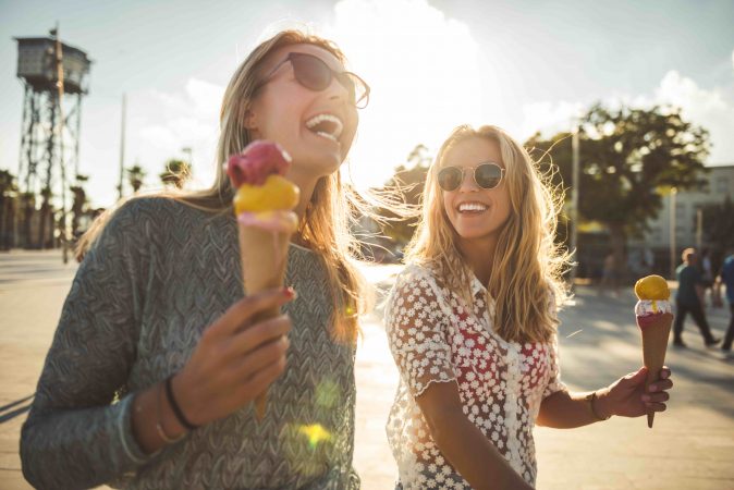 Zwei Frauen gehen in der Sonne spazieren und essen Eis in der Waffel.