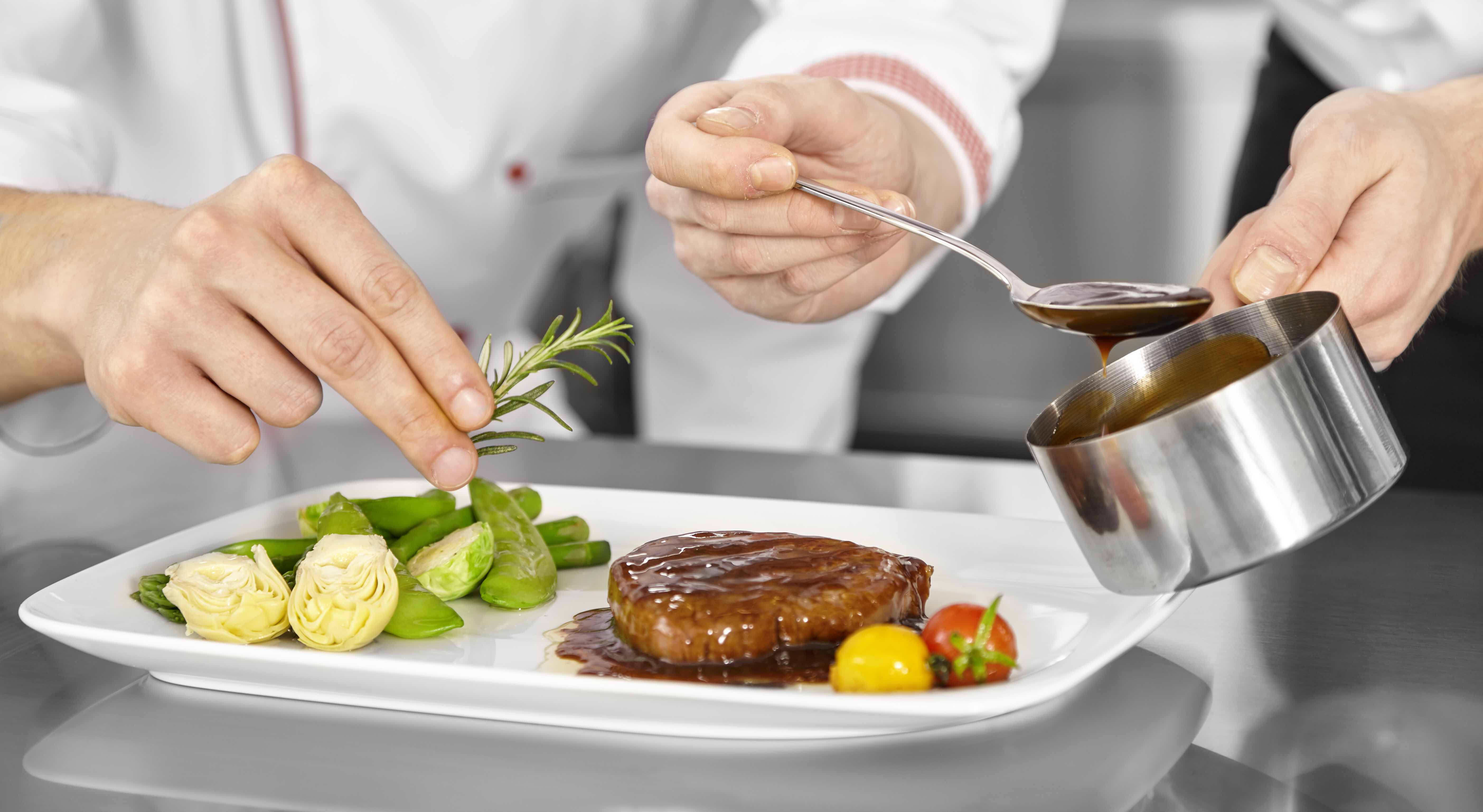 Köche richten ein Steak mit Rosmarin und Sauce an.