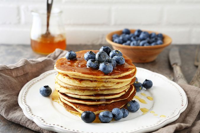 Frühstücksklassiker aus Kanada: Pancakes mit Ahornsirup und Blaubeeren auf einem weißen Porzellanteller angerichtet.