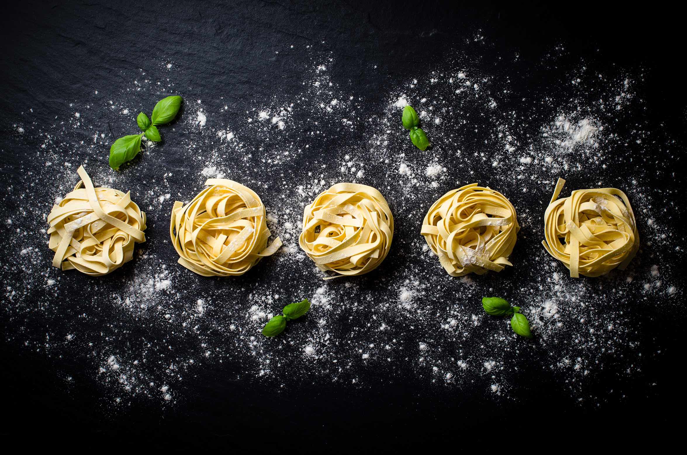 Pasta in Nestern drapiert auf einer Steinplatte, dekoriert mit Mehl und Basilikumblättern.
