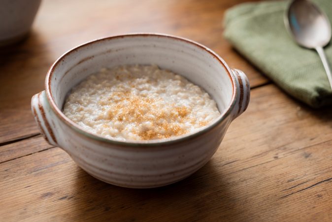 Porridge, bestreut mit Zimt, in einer Schüssel auf einem Holz-Untergrund.