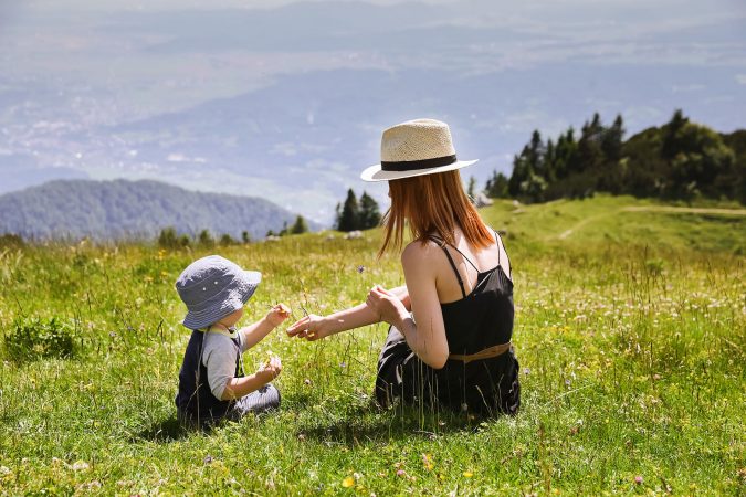 Frau sitzt mit Baby auf einer Kräuterwiese in den Bergen.