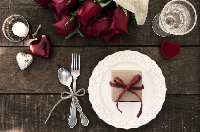 Gedeckter Valentinstagstisch mit roten Rosen, Dekoherzen und Geschenk